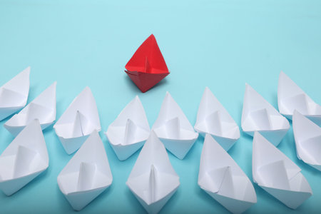 Leadership concept with red paper ship leading among group of white ships on white background