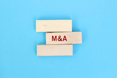 M and A merger and acquisitions concept. Male human hand pushing the wooden block with the word M...
