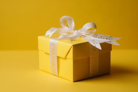 Yellow gift box tied with white ribbon on a yellow background. Copy spaceの素材