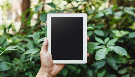 Hand holding digital tablet with blank screen and blur green leaves background.の素材