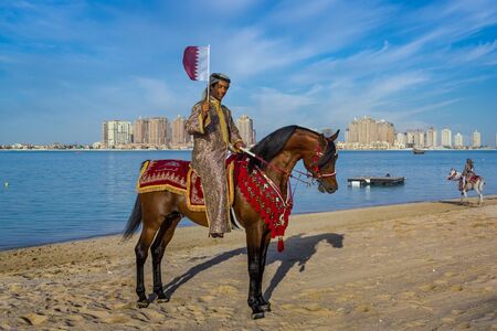 Doha,Qatar-December 18,2013: A Qatari man riding a horse and carry Qatar flag in Katara beach celebrating Qatar National Dayのeditorial素材