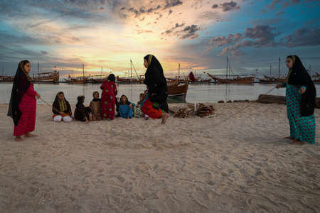 Doha,Qatar-December 3,2019: Qatari girls jumping rope in Katara beach at sunset with dhows in the water and clouds in sky in backgroundのeditorial素材