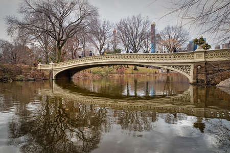 The bow bridge in central park, New York city daylight view with reflection in water , clouds, trees and Manhattan skyline in backgroundのeditorial素材