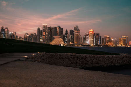 Doha Qatar skyline at night from  Museum of Islamic art garden showing skyscrapers lights reflected in the Arabic gulf with clouds in the sky in back groundのeditorial素材