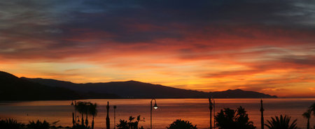 A very wide panoramic image showing a pretty and spectacular sunrise over sea and mountainsの写真素材