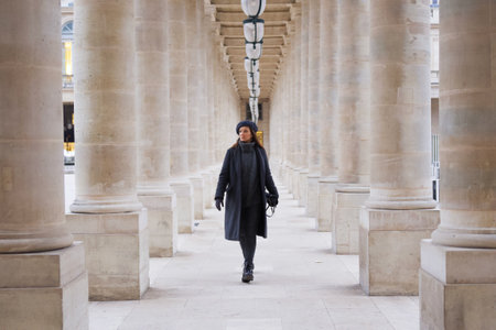 Chic Young Parisian Woman Strolling Through Palais Royal Columns in Franceの写真素材