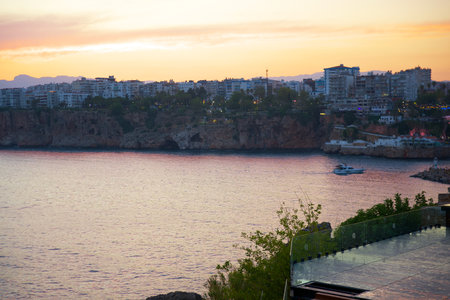 Colorful sunset over the coastal cliffs and cityscape with a yacht sailing on the calm sea in Antalya, Turkey.の写真素材