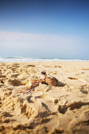 Pair of worn ballet shoes with ribbons lying abandoned on sandy beach shoreの写真素材