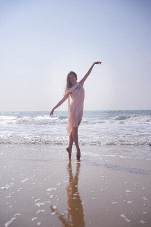 Ballet dancer on pointe in pink dress reflecting in wet sand by the ocean shoreの写真素材