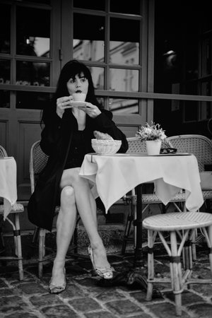 Elegant woman in monochrome scene drinking coffee at a Parisian cafe, evoking a timeless vintage...