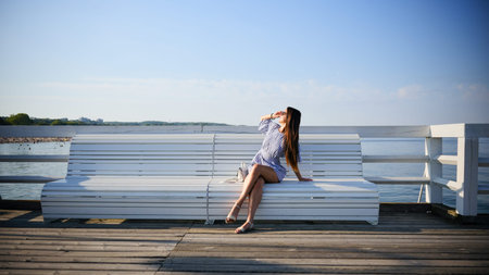 Young woman sitting on bench by the sea on sunny summer dayの写真素材
