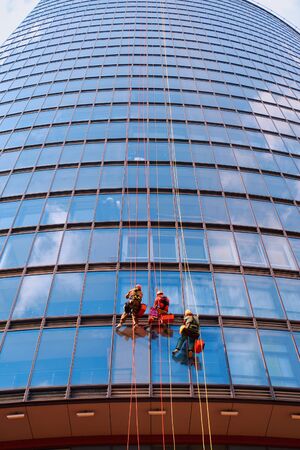 Three men workers in red and dark work clothes cleaning the exteriorの写真素材