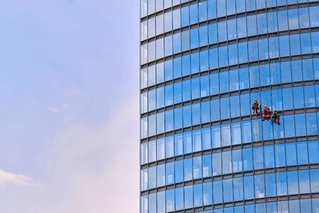 Mens workers in red and dark work clothes cleaning the exterior windows of a business skyscraper - industrial alpinismの写真素材