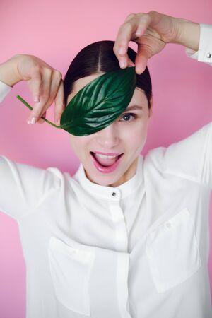 smiling girl in a white shirt with a flower in her hands on a pink backgroundの写真素材