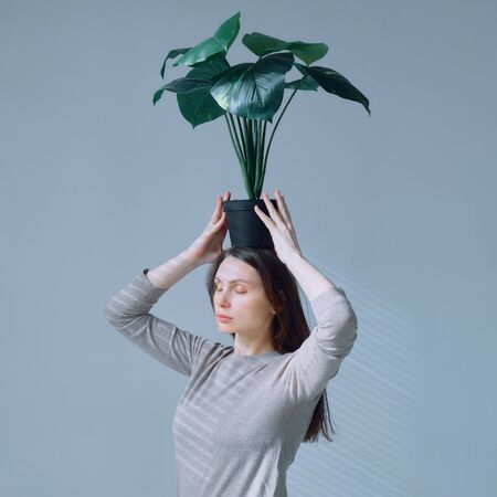 portrait of a young girl with a pot of flowers in her hands over her headの写真素材