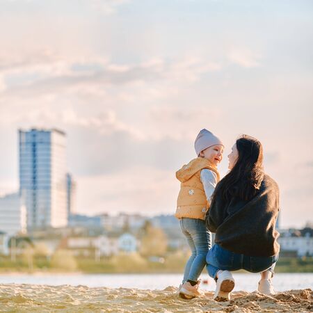 mom and daughter are standing with their backs on the beach against the backdrop of the city landscapeの写真素材