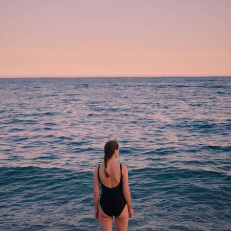 girl in a black swimsuit with her back to the seaの写真素材