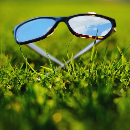 Sunglasses lying grass reflecting the blue skyの写真素材