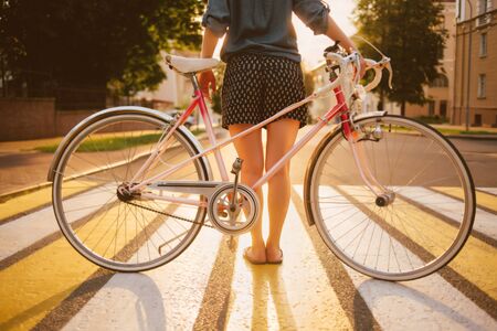 girl with a bicycle on city background in the sunlight, back viewの写真素材
