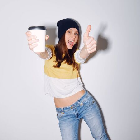 Closeup studio shot of pretty hipster teenage girl with beanie hat holding head making funny face. shows hand okの写真素材