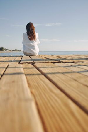 Woman sitting at the harbour on the quay with her back to the camera looking to sea. long dark hairの写真素材