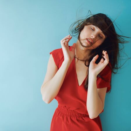 studio portrait of a girl in a red dress. fluttering brunette hairの写真素材
