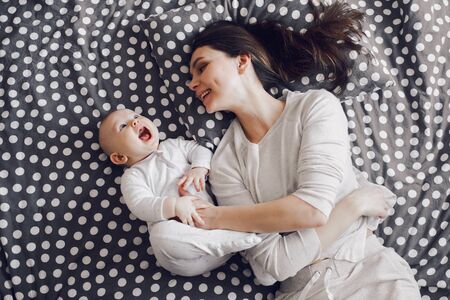 a young smiling mother plays with baby on a striped bedの写真素材