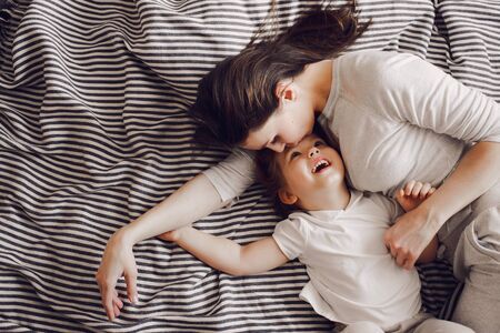 beautiful mother with 3 year old daughter hug and laugh while lying on the striped bedの写真素材
