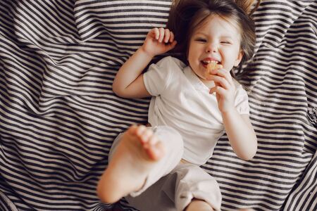 Portrait of beautiful cute little 3 years girl lying on bed in dress and looking at the cameraの写真素材