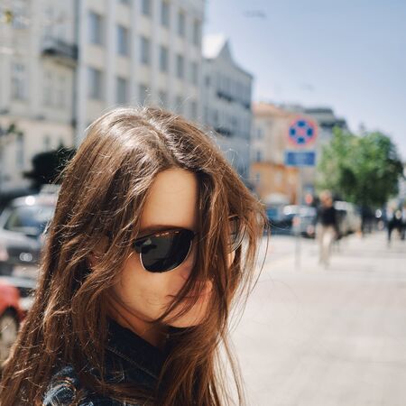 portrait of a girl in sunglasses against the background of the city with flying hair in the windの写真素材
