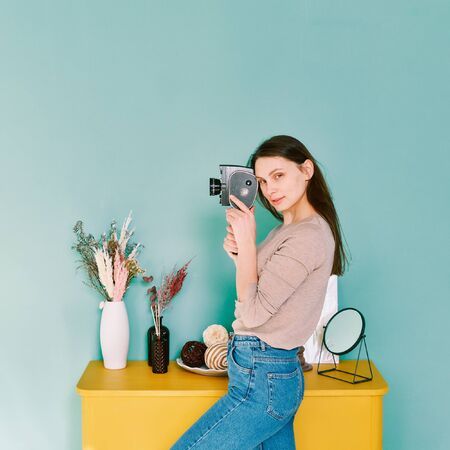 portrait of a girl in blue jeans with a retro camera th in hands on a turquoise background, look at the cameraの写真素材