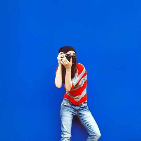 portrait of a beautiful girl with a camera on a red wall and blue doorの写真素材