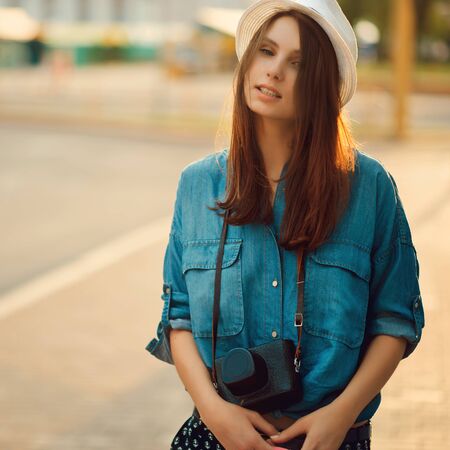 portrait of a young stylish woman in hat in morning sunshine with photo cameraの写真素材