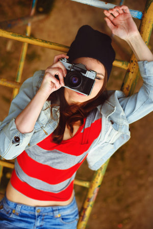 portrait of a beautiful girl in a cap and a denim jacket lying on the childrens slides and...
