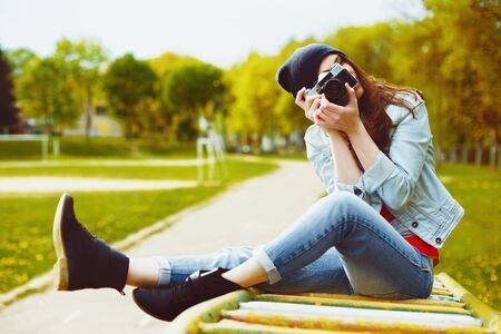 portrait of a beautiful hipster girl with a camera taking photos and sitting on a childrens slide in the parkの写真素材