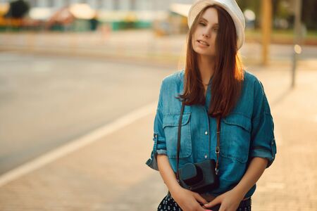 portrait of a young stylish woman in hat in morning sunshine with photo camera outdoorの写真素材