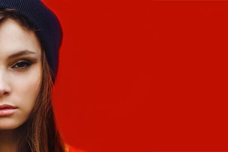portrait of a beautiful girl in hat and striped sweater on a red wall outdoorの写真素材
