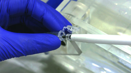Scientist's hand wearing blue glove using a pipette tool to take a liquid sample, Extreme close up....