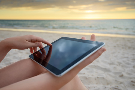 Woman holding a tablet on the beach during warm sunsetの写真素材