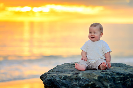 Cute smiling child sitting on the rock at sunsetの写真素材