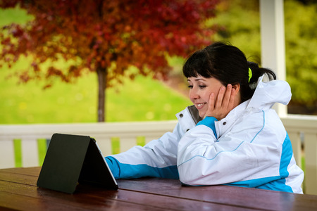 Women in the late twenties sitting with a tablet in the wooden arbor during the rainy autumn dayの写真素材