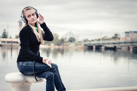 Girl with mobile phone and headphones enjoying music in the port. Toning effect appliedの写真素材