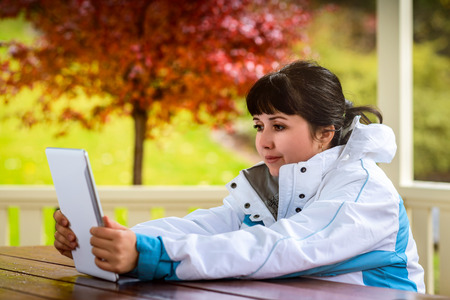 Woman sitting inside gazebo and holding tablet in autumn parkの写真素材