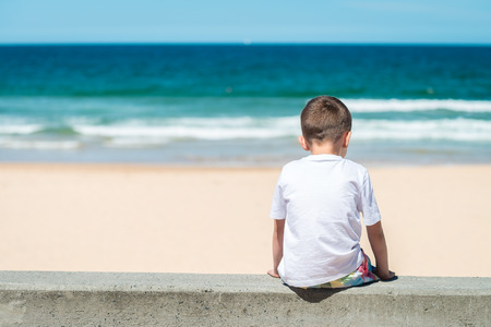 Sad boy sitting at he beach and thinking about somethingの写真素材