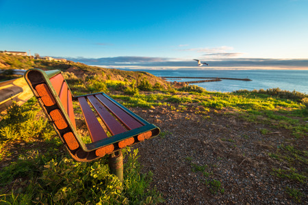 Bench at the edge of the cliff at sunset with clouds above the sea, South Australian shoreの写真素材