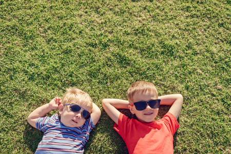 Happy smiling kids relaxing on green grass under sun, top view with copy space. Color-toning appliedの写真素材