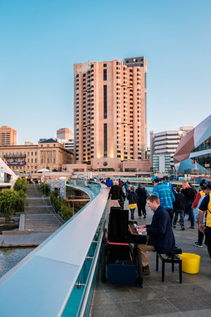 Adelaide, Australia - September 11, 2016: Man playing piano and people walking through Torrens foot bridge from Adelaide Oval after game in Adelaide city centre at sunsetのeditorial素材