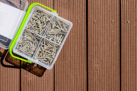 Assorted screws in plastic box on wooden brown deck