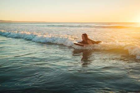 Woman riding a bodyboard at sunset, Moana Beach, South Australiaの写真素材