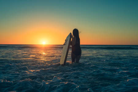 Woman with bodyboard enetering the water to catch some waves at Moana Beach during sunset in South Australiaの写真素材